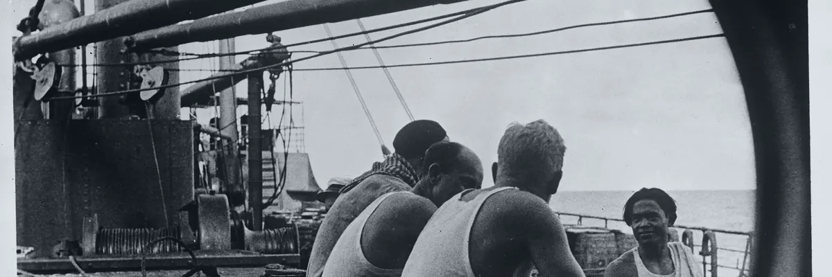 Black-and-white archive photo of merchant seamen sitting on deck during a short break, rigging and davits behind them