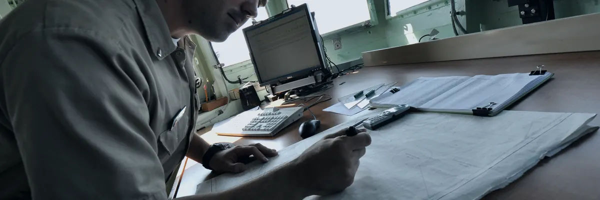 Third mate studying navigational charts at the chart table on the bridge of a ship