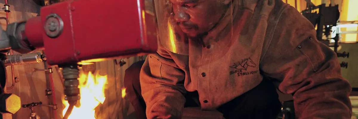 Merchant mariner in a welding mask and leather gloves welding a steel fitting in a ship's workshop, sparks flying